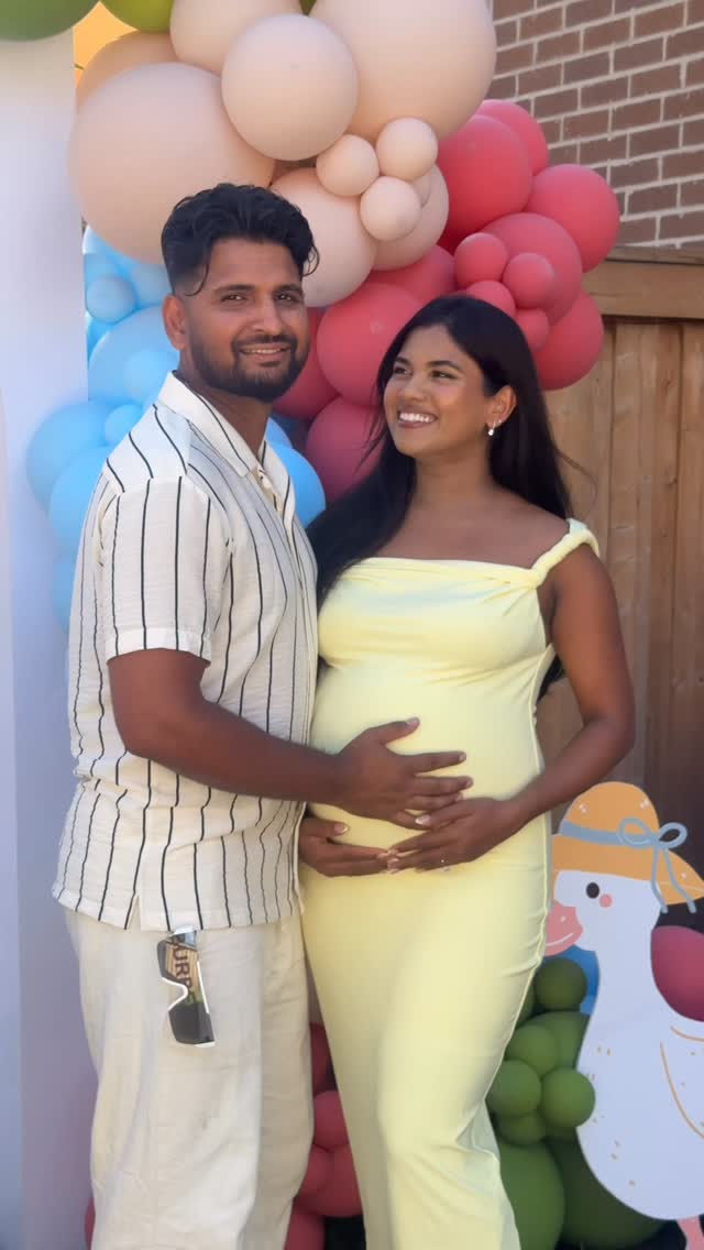 Parents-to-be smiling together in front of a colourful balloon backdrop